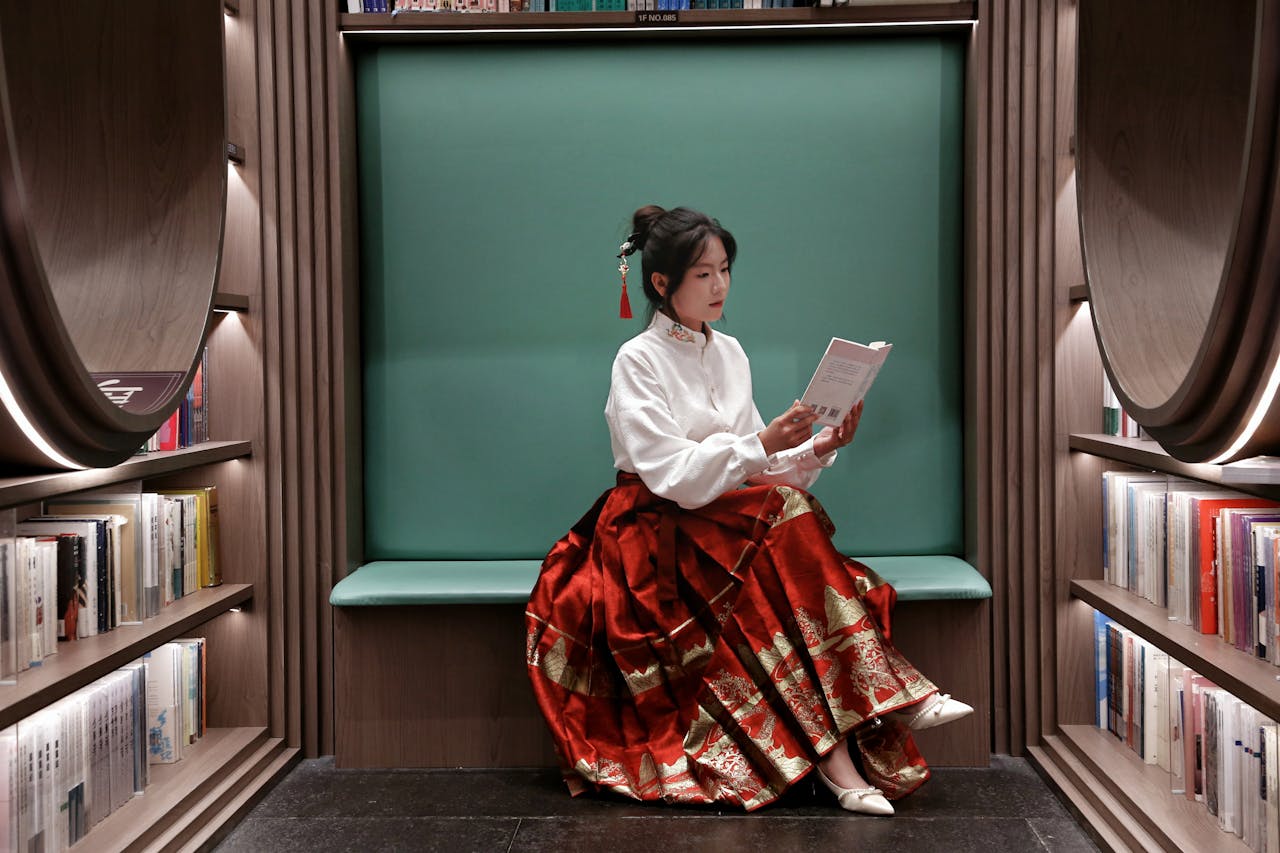 A person reading a book in a stylish red skirt in a cozy library alcove.